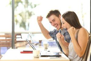 Group of two young euphoric students watching exam results in a laptop in a table of an university campus bar